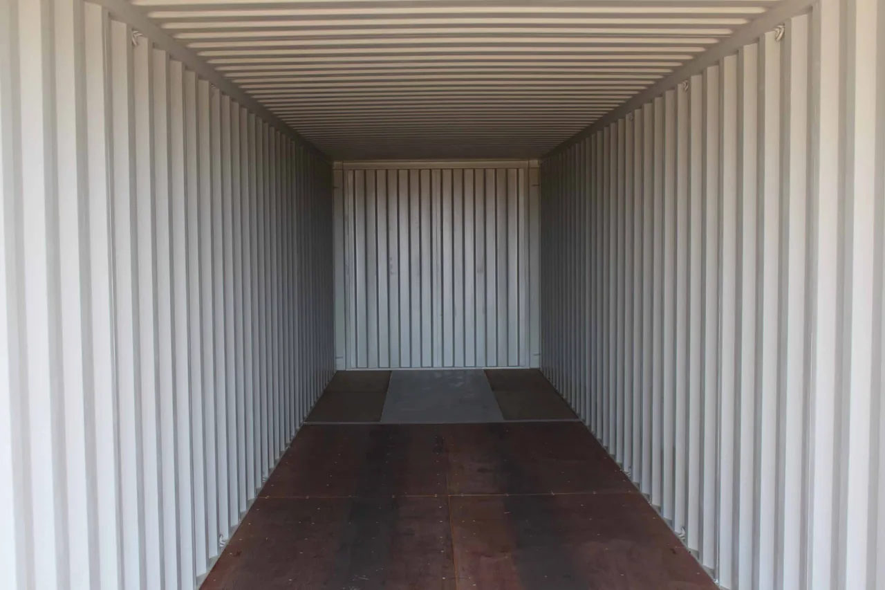 Empty container interior showing bare corrugated steel walls and plywood floor before shelving installation